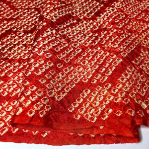 May include: A vibrant red fabric featuring a textured, crinkled surface with a repeating pattern of small, off-white, square-shaped outlines arranged in diagonal rows across the material, creating a distinct visual contrast and depth.
