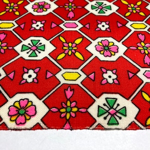 May include: Red fabric with a white and green geometric pattern. The pattern features small pink flowers, green crosses, and yellow hexagons.