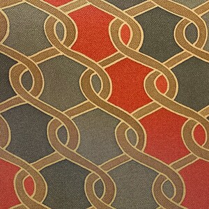 May include: Close-up of a repeating pattern featuring interwoven, curved lines in a warm brown hue, set against a backdrop of red, gray, and dark gray diamond shapes. The design has a textured appearance.