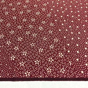 May include: A close-up of a burgundy fabric with a white floral pattern. The fabric has a subtle texture and a slightly shiny finish.