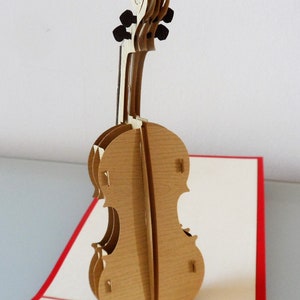 May include: A brown wooden pop-up card featuring a cello. The card is open and the cello is standing upright.