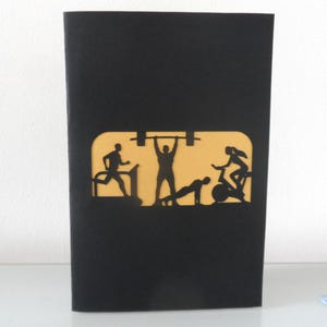 Peut inclure: Carte de v&oelig;ux noire avec un motif d&eacute;coup&eacute; repr&eacute;sentant des silhouettes de personnes faisant de l'exercice. Le motif comprend une personne courant sur un tapis roulant, soulevant des poids, faisant des pompes et faisant du v&eacute;lo. Le fond est jaune.