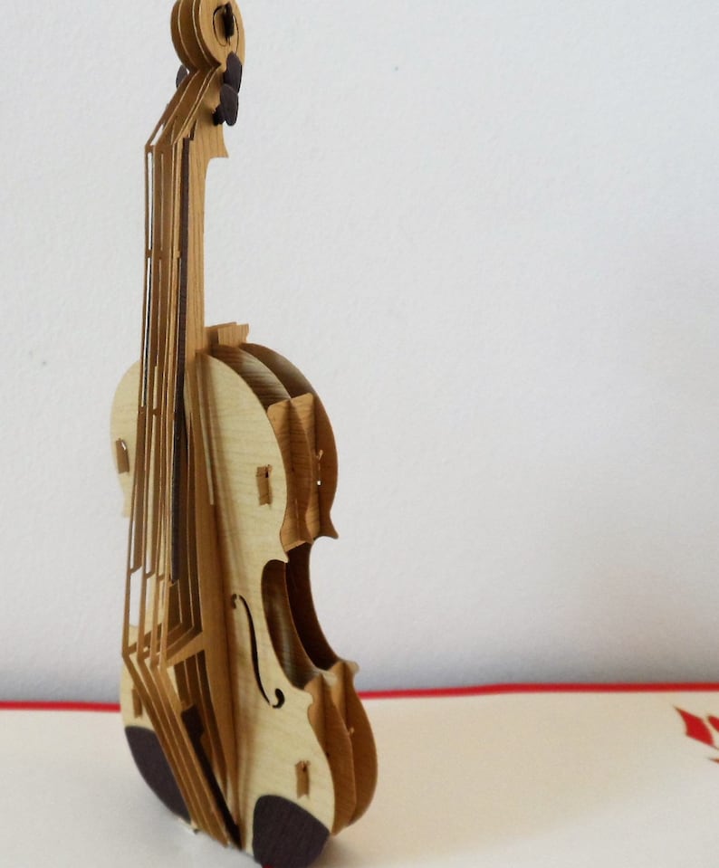 May include: A wooden pop-up card featuring a detailed model of a violin. The violin is made of light brown wood and has a dark brown finish on the bottom.