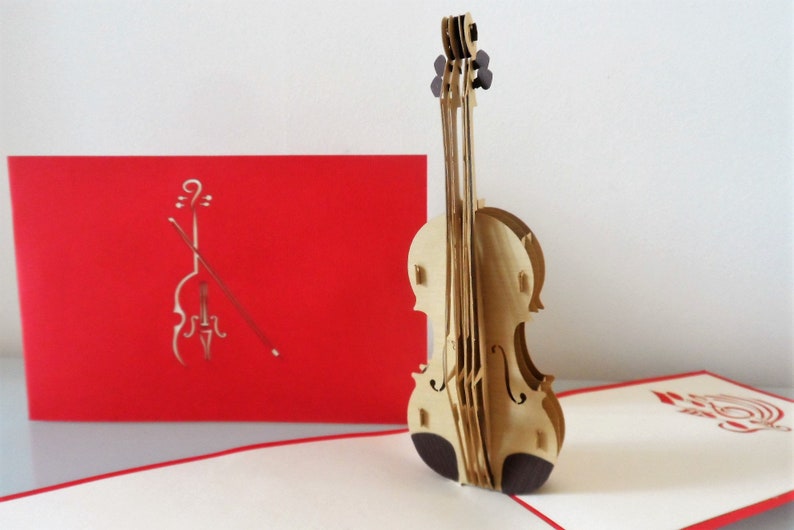 May include: A 3D pop-up card featuring a wooden violin. The card is open and the violin is standing up. The front of the card is red with a cutout of a violin and bow.