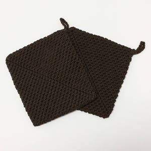 May include: Two dark brown, square potholders made of a knitted material. Each potholder has a small loop at one corner for hanging. The potholders are designed for kitchen use.