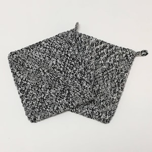May include: Two square, hand-knitted potholders in a black, white, and gray speckled pattern. Each potholder has a small loop at one corner for hanging. The potholders are made of a thick, textured yarn.