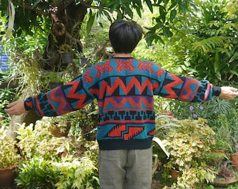 May include: A person wearing a blue, red, and black patterned sweater with geometric designs. The sweater has long sleeves and a crew neck.