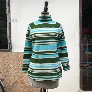 May include: A striped turtleneck sweater in green, white, and blue. The sweater is on a mannequin.