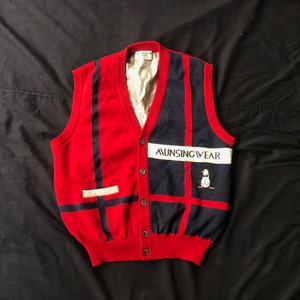 May include: A red and blue striped knitted vest with a white pocket and a penguin logo that says "Aunsingwear".