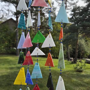 May include: A hanging mobile featuring multiple strands of triangular glass pieces in various colors including red, blue, green, yellow, white, and orange. The glass triangles are connected by thin wire and small blue beads, suspended from a wooden bar.