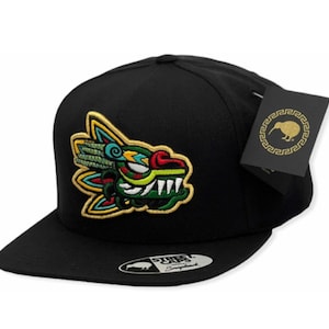 May include: Black snapback hat with a colorful embroidered Aztec-inspired design on the front. The design features a detailed, stylized creature with green, yellow, and blue accents. A tag with a kiwi bird logo hangs from the side.