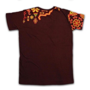 Pu&ograve; includere: Una t-shirt marrone scuro con intricati ricami geometrici nei toni dell'arancione, giallo e rosso. Il design &egrave; concentrato sulle spalle e sulla manica, creando un contrasto visivo sorprendente con il tessuto tinta unita.