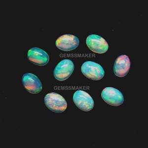 Peut inclure: Plusieurs opales ovales aux couleurs irisées, notamment bleu, vert, jaune et rose, sur fond noir. Le texte "GEMSSMAKER" est visible sur l'image.