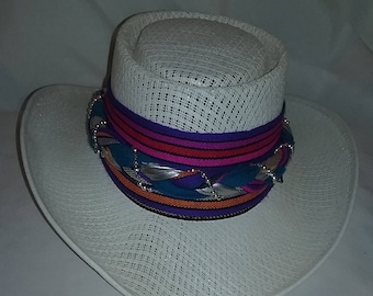 May include: A white straw hat with a wide brim and a colorful ribbon band. The ribbon is decorated with silver beads and has stripes of purple, pink, orange, and blue.