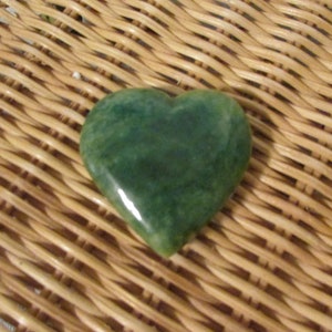 May include: A heart-shaped green stone on a woven wicker surface.