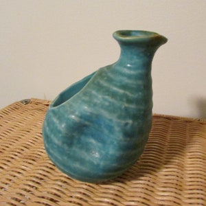 May include: A teal blue ceramic vase with a textured surface and a wide opening. The vase has a unique, organic shape.