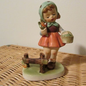 Figura vintage de una niña con flores y una cesta junto a una valla, figura vintage estilo Hummel