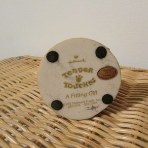 Puede incluir: Figurita de cer&aacute;mica blanca con una inscripci&oacute;n dorada que dice "Hallmark Tender Touches A Fitting Gift 1992 Hallmark Cards, Inc. QEC6354 QHG7065" y un c&iacute;rculo dorado con el texto "Made in China".
