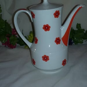 May include: White ceramic teapot with an orange and red floral design. The teapot has a lid and a handle.