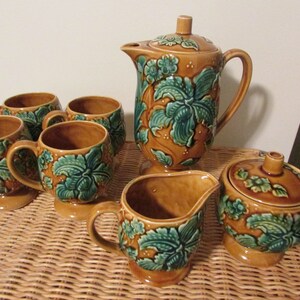 Op de afbeelding: Een vintage theeservies met een bruin en groen bloemenmotief. De set bevat een theepot, een roomkan, een suikerpot en vier kopjes.