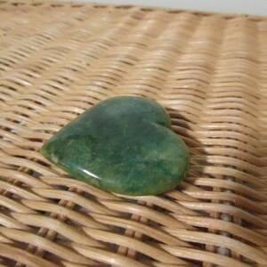 May include: A green heart-shaped stone on a woven wicker surface.