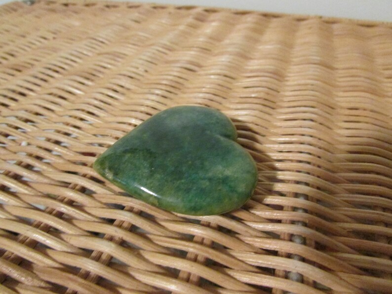 May include: A green heart-shaped stone on a woven wicker surface.