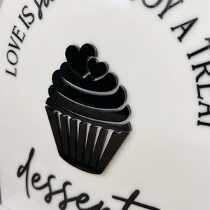 May include: White sign with black text and a black cupcake graphic. The text reads "Love is sweet. Enjoy a little dessert bar."