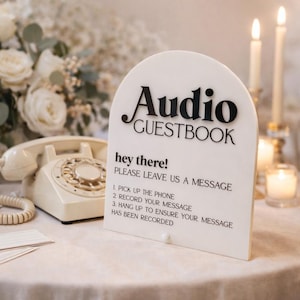 May include: A white Audio Guestbook sign with black lettering, including the words "Audio Guestbook" and instructions. A vintage cream-colored telephone sits nearby. The sign reads "Hey there! Please leave us a message."