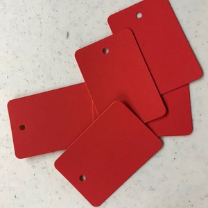 May include: Four red rectangular tags with a hole punched in the top center of each tag.