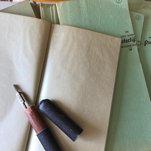 May include: A close-up of a vintage book with a compass and two black pencil holders on top of the open pages. The book is green and has the text "Mint Stationery Protective" printed on the cover.