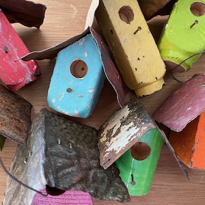 May include: A collection of colorful, rustic birdhouses made of wood and metal. The birdhouses are painted in various colors, including red, blue, green, yellow, and orange. Some of the birdhouses have a distressed look, while others are more polished. The birdhouses are all different shapes and sizes, and they would make a charming addition to any garden or home.