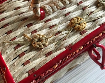May include: A vintage woven basket with a red trim and handle. The basket features a natural, light-colored weave with red accents and decorative woven details. The handle is made of twisted natural fibers.