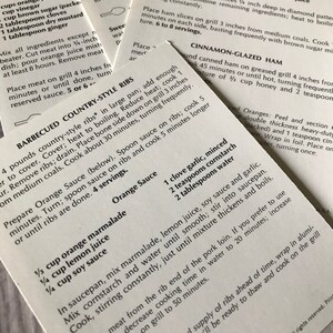 May include: A close-up of a recipe card for barbecued country-style ribs. The recipe includes instructions for preparing the ribs, as well as a recipe for an orange sauce. The recipe card is printed on white paper with black text.