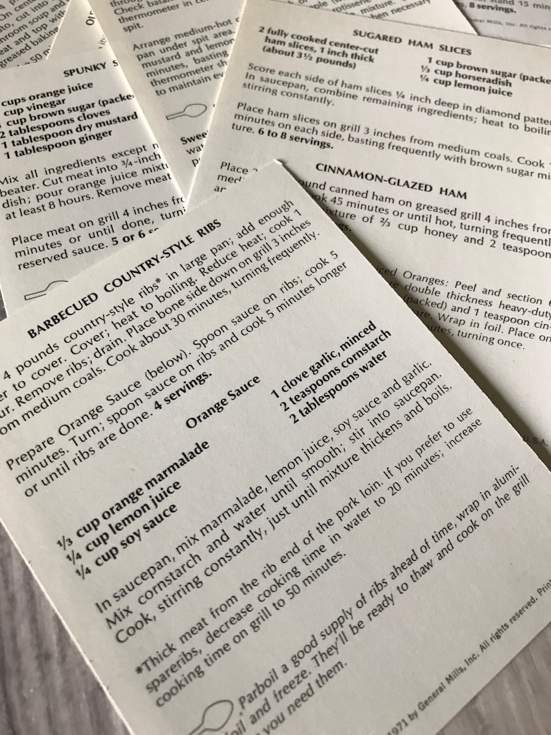 May include: A close-up of a recipe card for barbecued country-style ribs. The recipe includes instructions for preparing the ribs, as well as a recipe for an orange sauce. The recipe card is printed on white paper with black text.