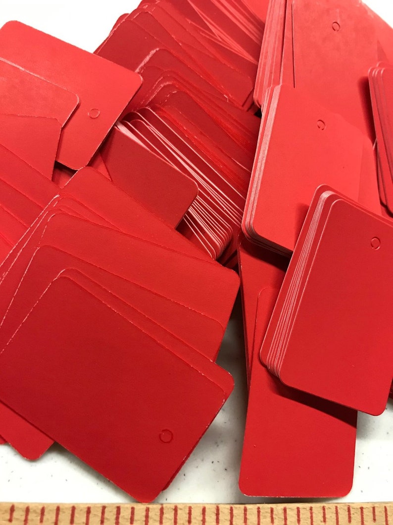 May include: A stack of bright red rectangular gift tags with a hole punched in the top corner. The tags are made of a sturdy cardstock and are ready to be used for gift wrapping.