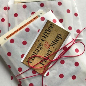 May include: A white paper bag with red polka dots is tied with a red string. The bag contains a stack of paper and a business card that reads "The Vintage Office & Paper Shop est. 2017".