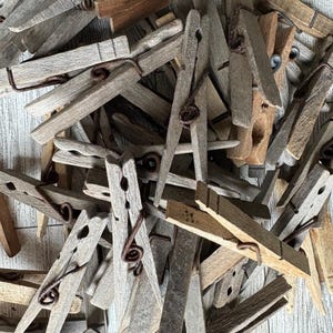 May include: A pile of rustic wooden clothespins with metal springs. The clothespins are weathered and have a natural, vintage look.