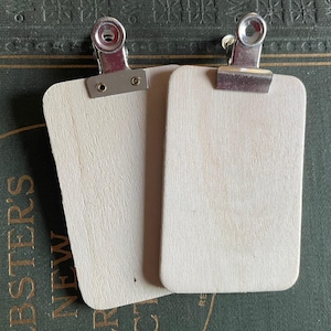 May include: Two blank wooden clipboard signs with silver metal clips. The signs are rectangular and have a light wood grain finish.