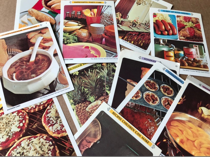 May include: A collection of recipe cards featuring various dishes, including onion soup, pizza, pineapple, and a variety of desserts. The cards are from "The Betty Crocker Recipe Card Library" and feature different categories like "International Favorites", "Impromptu Party Fare", "Hunky Up Main Dishes", "Fondues", "Convenient", "Outdoor", and "Recipes Children Can Make".
