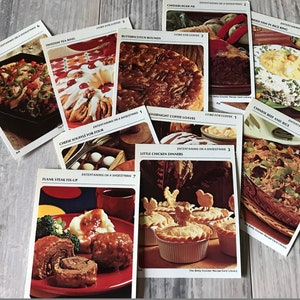 May include: A collection of recipe cards featuring various dishes, including Creole Flounder, Swedish Tea Ring, Butterscotch Rounds, Cheeseburger Pie, Fried Fish in Rice Ring, Chinese Beef and Rice, Overnight Coffee Loaves, Little Chicken Dinners, and Flank Steak Fix-Up. Each card has a photo of the dish and the title of the recipe. The cards are all from the Betty Crocker Recipe Card Library.