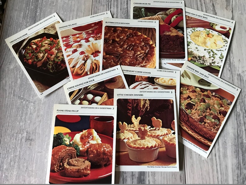 May include: A collection of recipe cards featuring various dishes, including Creole Flounder, Swedish Tea Ring, Butterscotch Rounds, Cheeseburger Pie, Fried Fish in Rice Ring, Chinese Beef and Rice, Overnight Coffee Loaves, Little Chicken Dinners, and Flank Steak Fix-Up. Each card has a photo of the dish and the title of the recipe. The cards are all from the Betty Crocker Recipe Card Library.