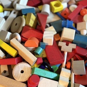 May include: A large collection of wooden building blocks in various geometric shapes and sizes. The pieces feature a mix of natural wood finishes and painted surfaces in primary colors including red, blue, yellow, green, and orange.