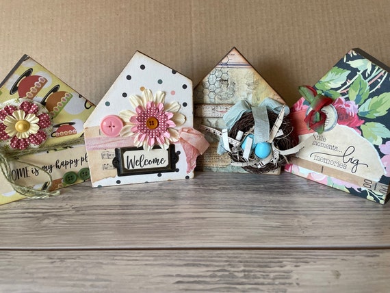 Tiny mixed-media collage houses built from layered found materials — each one is a genuinely one-of-a-kind miniature world a real human assembled by hand.