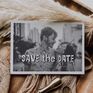 May include: Black and white save the date card featuring a couple, with the text "SAVE the DATE". Includes a gold wax seal stamp and three wax seals with a floral design. The card is on a wooden surface.