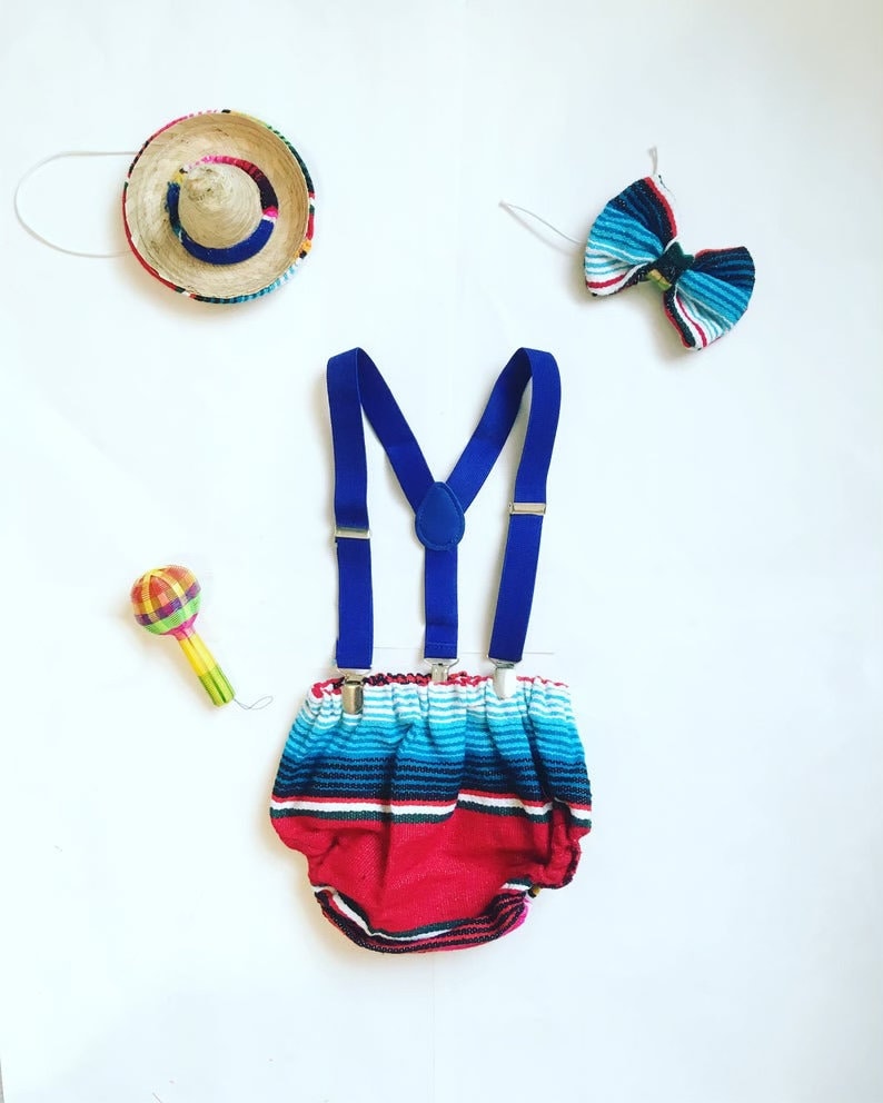 K&ouml;nnte beinhalten: Ein Baby-Outfit f&uuml;r eine Fiesta-Mottoparty. Das Outfit beinhaltet eine rote und blaue gestreifte Windelh&uuml;lle, blaue Hosentr&auml;ger, eine blaue und wei&szlig;e gestreifte Fliege, eine Rassel und einen Sombrero.