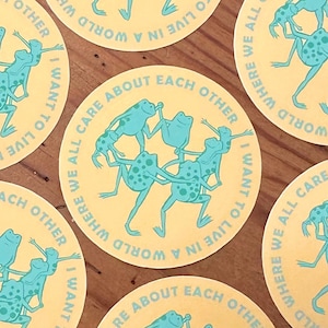 May include: Six round stickers with a yellow background and blue frogs. The text on the stickers reads "I want to live in a world where we all care about each other".