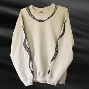 Op de afbeelding: Een beige sweatshirt met een zwart slangontwerp op de voorkant en mouwen.