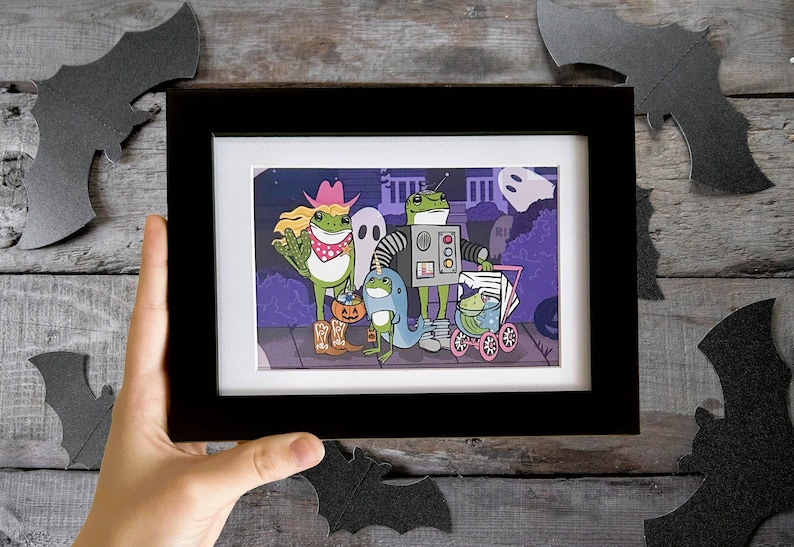 K&ouml;nnte beinhalten: Eine gerahmte Illustration einer Gruppe von Fr&ouml;schen, die sich f&uuml;r Halloween verkleidet haben. Die Fr&ouml;sche sind als Cowboy, Roboter, Narwal und Baby im Kinderwagen verkleidet. Die Illustration ist vor einem violetten Hintergrund mit einem Friedhof im Hintergrund.