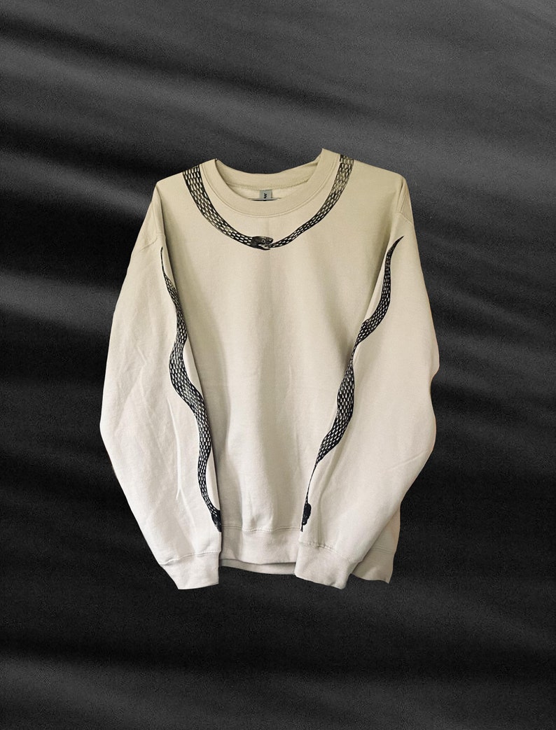 Op de afbeelding: Een beige sweatshirt met een zwart slangontwerp op de voorkant en mouwen.