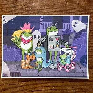 K&ouml;nnte beinhalten: Vier gr&uuml;ne Froschfiguren, die sich f&uuml;r Halloween verkleidet haben. Ein Frosch tr&auml;gt einen Cowboyhut und tr&auml;gt einen K&uuml;rbis-Eimer. Ein anderer Frosch tr&auml;gt ein Roboterkost&uuml;m und tr&auml;gt einen Eimer. Ein dritter Frosch tr&auml;gt ein blaues und wei&szlig;es Kost&uuml;m und tr&auml;gt einen Eimer. Der vierte Frosch sitzt in einem rosa Kinderwagen.